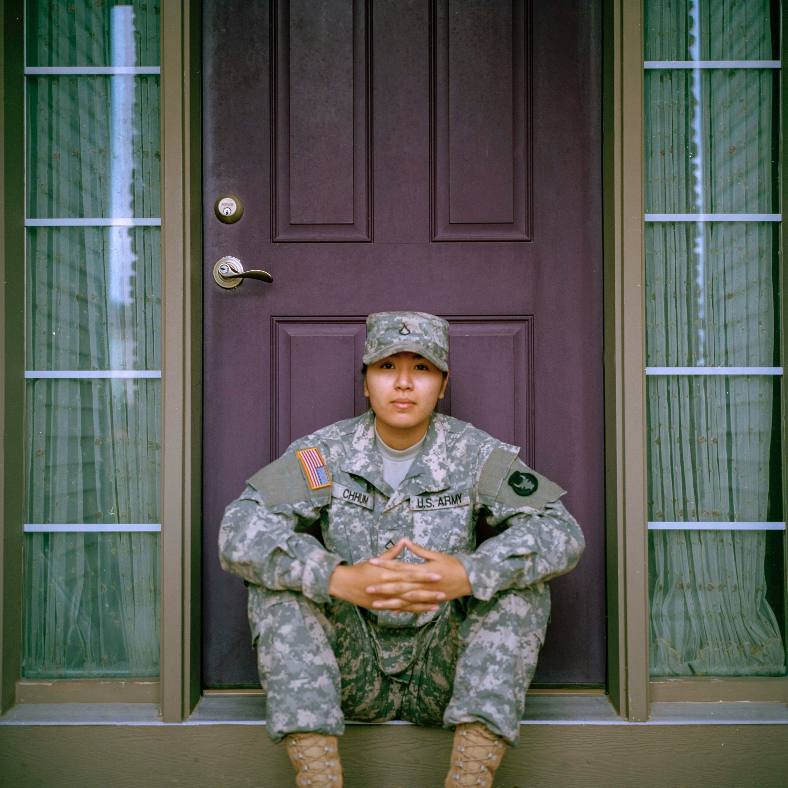 Army Woman Sitting in Front of Front Door Army woman in uniform sitting thoughtfully in front of a residential front door.